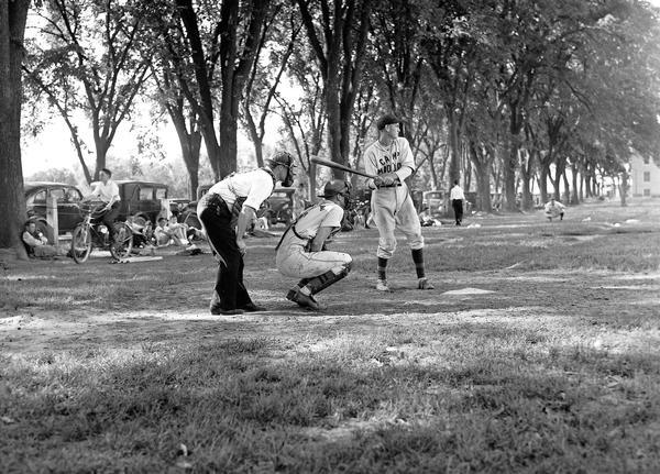The catcher squats as the batter gets ready to swing at a pitch while the umpire looks on.  This image was taken as part of the WPA Federal Writers Project.