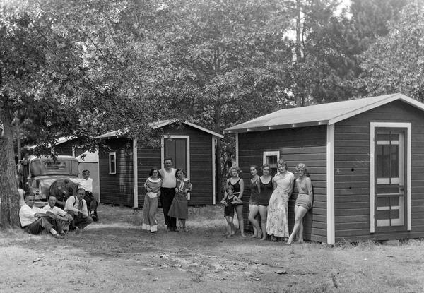 Women, men and children in summer clothes stand between cabins at the Gallop Inn on Tainter Lake.