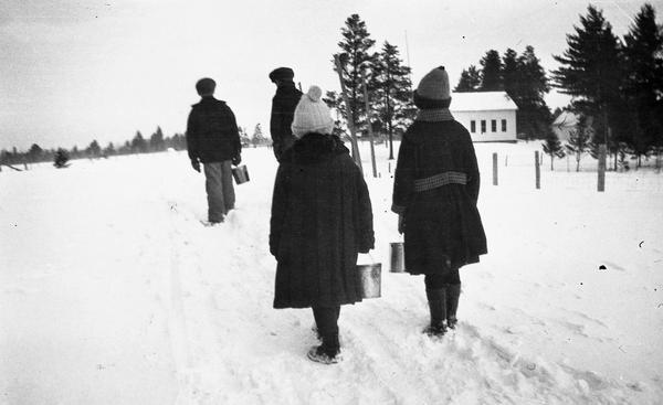 Winter scene with children bundled-up against the cold carrying their lunch pails down a snowy rural path to the one room school house called the Pahquahahwong school.