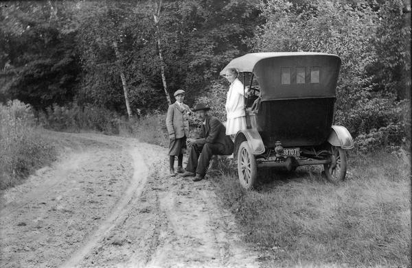 Carl Peterson and his family, take a rest while driving their car on a rural dirt road. His son's name is Laurie and the girl is Muriel Peterson Jacobs. Often Carl would take his children with him while looking for telephone line breaks. Noted: "Photograph by Mrs. Carl Peterson."