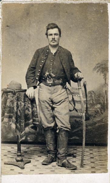 Studio portrait of Thomas J. Handy, Company F, 4th Wisconsin Cavalry, standing with sword and pistol in belt.