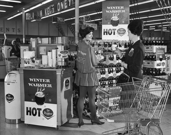 Costumed saleswoman at a supermarket display for Dr. Pepper soft drinks. The display includes samples of "Hot Dr. Pepper" and "winter warmer."