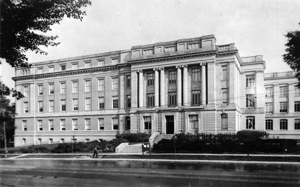 Exterior of the Thomas C. Chamberlain Hall of the Chemistry Building  at the intersection of University Avenue and North Charter Street. There is a signboard by the front steps and a man cutting the grass with a push mower.