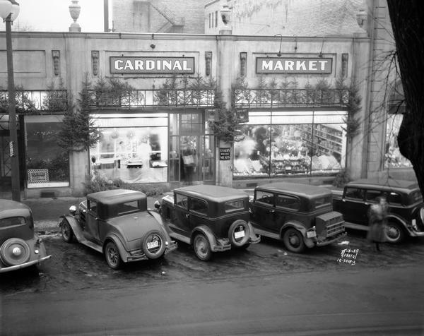 Elevated view of automobiles parked in front of the Cardinal Market at 120 North Fairchild Street, with a sign on the storefront advertising Essers Wholesale Meats.