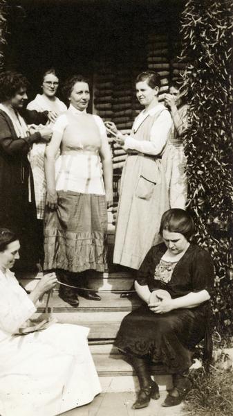 Dressmaking instruction outdoors, with one woman serving as a model.