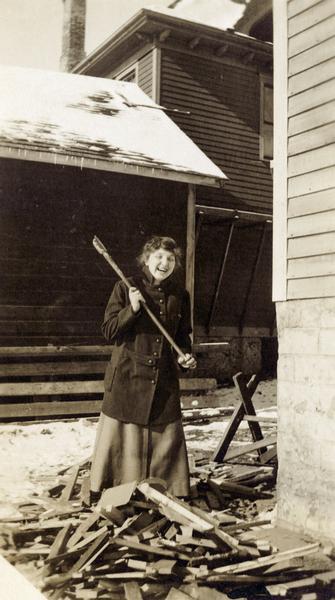 A smiling woman holding an axe holding a pose while chopping wood.