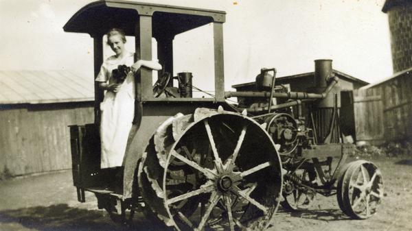 Woman holding flowers posing on the back of an Avery gasoline tractor.