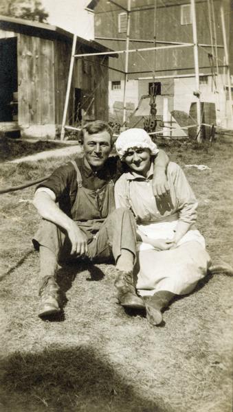 Farm couple seated together outdoors on the lawn, his arm around her shoulders.
