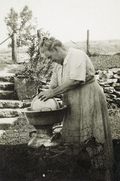 A woman washing dishes outdoors in a washtub.