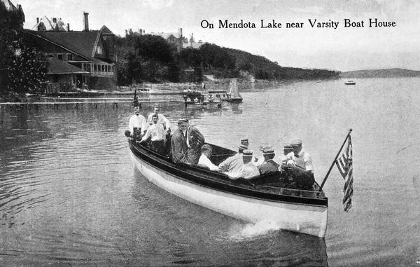 View of a group of people in a large model launch with an American flag on Lake Mendota near the University of Wisconsin-Madison boathouse.