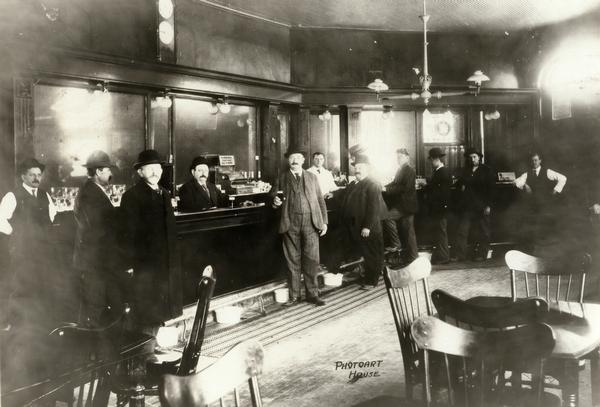 Interior view of the Hausmann Brewery Bar with spittoons on the floor. A sign behind the bar reads: "No intoxicating drinks sold to minors." The patrons and bartender are all men.
