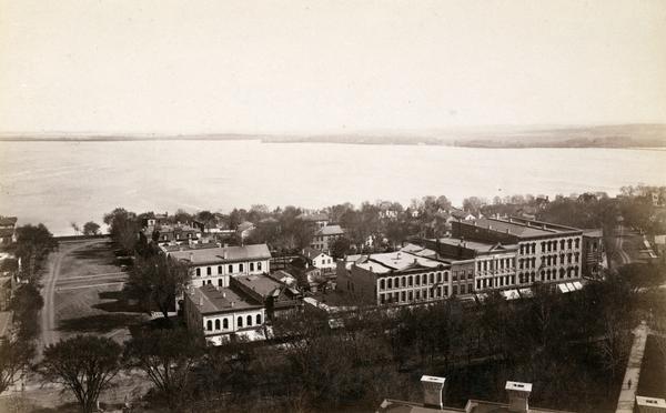 Looking south from the capitol dome of the Wisconsin State Capitol, the view is of West Main Street bound by South Hamilton Street and Monona Avenue (now Martin Luther King Jr. Boulevard). None of these buildings remain. They have been replaced by city, county, and state office buildings. Lake Monona is in the background.
