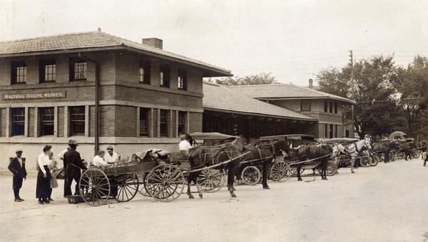 Exterior view of the Municipal Market, which was built in 1910 but not operated successfully until July 1917 when it was run by a group of women from the Dane County Council of Defense Food Board. There are horses and wagons lined up in front of the building, and a sign on the building reads: "Waiting Room, Women."