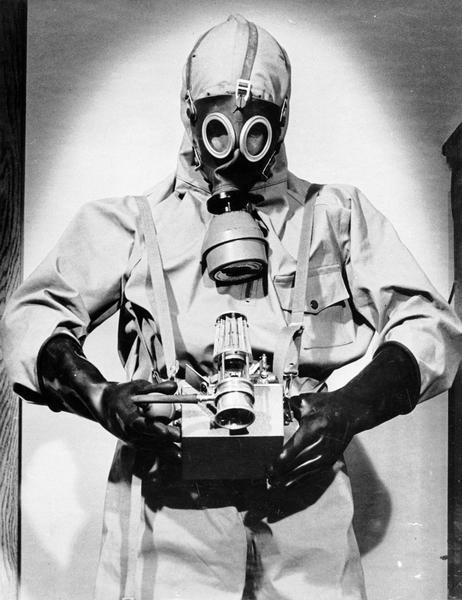 Charles L. Senn wearing a gas decontamination suit and gas mask and holding a gas detector, probably during World War II.