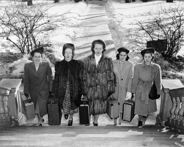 Five women walking up a flight of stairs dressed in civilian clothing and carrying suitcases reporting for duty as WAVES (Women Accepted for Volunteer Emergency Service), probably at the University of Wisconsin, Madison.