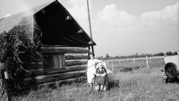 Mrs. Ollie Jacobs and her daughter Pearl Jacobs Borusky outdoors near a log building.