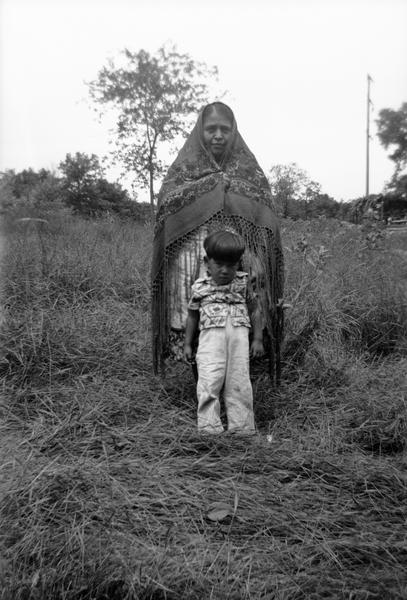 Unidentified woman and child (Marie Shekah and Bernard Sheka?) standing outdoors. Probably at Winnebago (HoChunk) Indian Village.