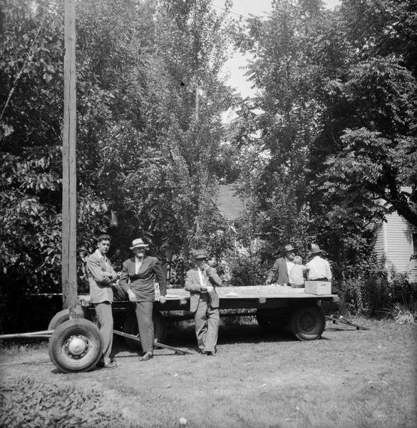 Five men and a young child gathered around flat-bed trailer.