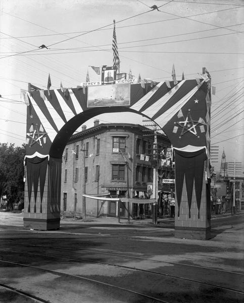 Wisconsin Semi-Centennial ceremonial archway erected at State and Mifflin Streets to celebrate Admiral George Dewey's victory over the Spanish fleet at Manila Bay in the Philippines during the Spanish-American War. The State Saloon is visible through the archway, on the 100 block of State Street.