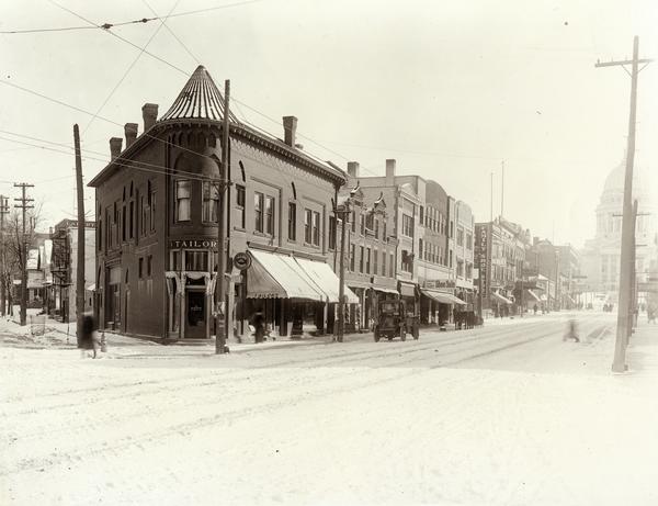 View of the 200 block of State Street, northside, with Tailors and Gents Furnishers, John Ripp's Great Unloading Shoe Sale, and the Wisconsin State Capitol in the background.