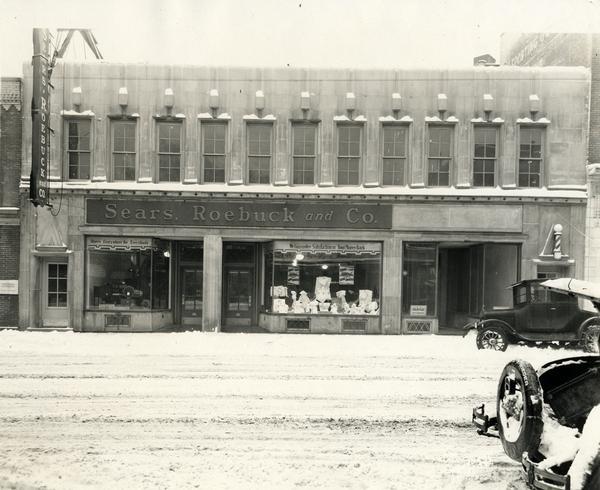 Storefront of Sears, Roebuck and Co. on State Street, with snow-covered streets and snow topped automobiles.