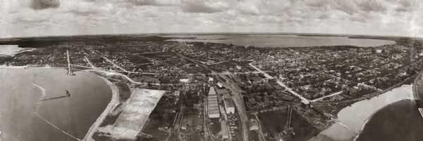 A panoramic aerial view of the Isthmus taken from a kite. Lake Mendota is to the right in the background with Picnic Point jutting into the lake. The photograph was taken over the point where the two railroad tracks criss-crossed Monona Bay.