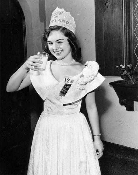 Marjean Czerwinski, the 1951 Alice in Dairyland, wearing her crown, and taking a drink of milk while winking at the camera.