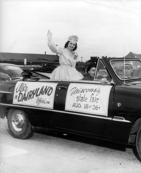 Marjean Czerwinski, the 1951 Alice in Dairyland, rides in the official Alice car with Mr. and Mrs. Wing during the Army Day Parade at the Wisconsin State Fair.