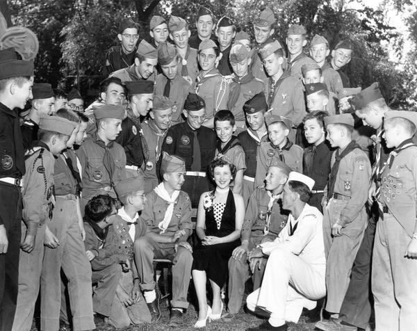 Mary Ellen Jenks, the 1953 Alice in Dairyland, visits a Boy Scout camp, where she is surrounded by admiring scouts and a member of the navy.