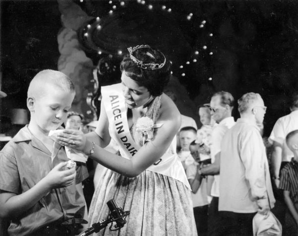 Merrie Barney, the 1959 Alice in Dairyland, helps a young boy eating a cream puff, always a favorite treat at the Wisconsin State Fair.