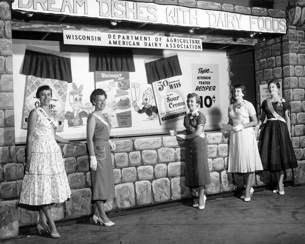 The 1955 Alice in Dairyland, Barbara Brown, stands with four Alice Princesses in front of a Wisconsin Department of Agriculture/American Dairy Association display promoting dairy products.