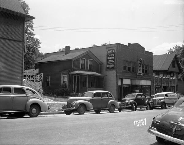 Automobiles and Pattersen's delivery truck parked in front of businesses along the 200 block of West Mifflin Street. Shown, left to right, are Sam Corona's Beauty Salon (203), Mahoney Sisters Dressmakers (205), Pattersen's Floor Coverings (209), Photo Copy Service (211), and apartment house (215).