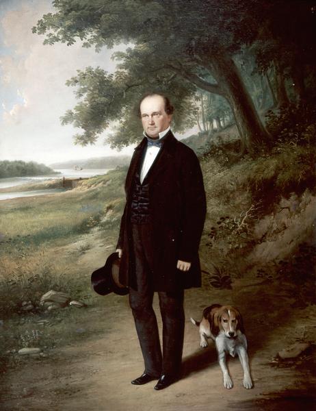 Full-length portrait of Morgan L. Martin standing in a landscape, with a dog sitting at his feet.