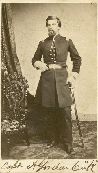 Full-length studio portrait of Alexander Gordon Jr., Company K, 7th Wisconsin Infantry. He has a sword on his left side.