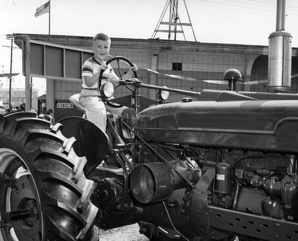 A boy sits in the seat and takes the steering wheel of a shiny new tractor at the Wisconsin State Fair.