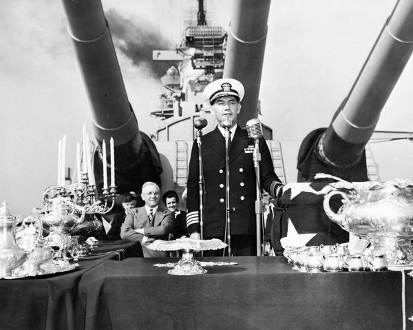 Captain Roper of the USS Wisconsin speaking aboard ship at a presentation ceremony of a silver service from the people of Wisconsin to the battleship. Governor Oscar Rennebohm is visible on the left.