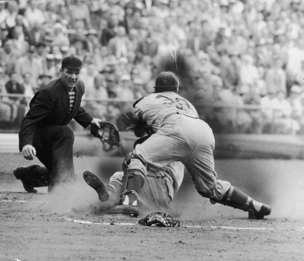 Baseball player sliding into base as the umpire looks on.