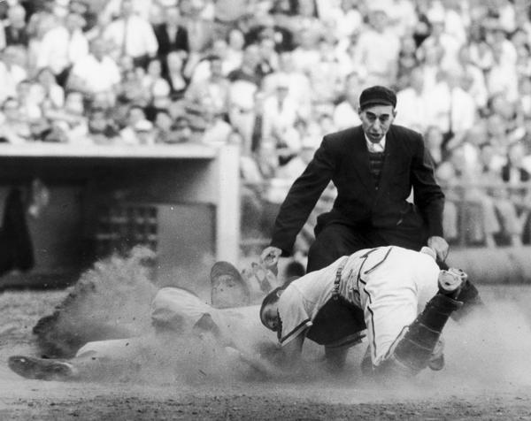 A baseball player sliding into home plate as the umpire is looking on.