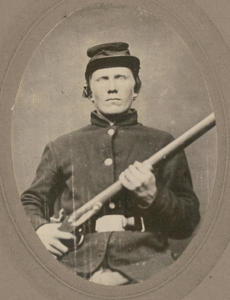 A seated, waist-up studio portrait of Erick Larson, a corporal in Company B, 15th Wisconsin Infantry, in uniform holding a musket across his chest.  The following information was obtained from the Regimental and Descriptive Rolls, Volume 20: He resided  Deerfield, Wisconsin. On October 22, 1861, he enlisted in Madison, Wisconsin and on November 16, 1861, he was mustered into service in Madison, Wisconsin at the age of 24. On enlistment he held the rank of corporal. He was wounded in the head and shoulders on May 27, 1864, during the fighting on Altoona Hills near New Hope Church, Georgia. He was moved to a general hospital in Chattanooga, Tennessee where he died from his wounds on June 22, 1864.  He is buried at the Chattanooga National Cemetery: Section E, Site, 11445, Grave 248.