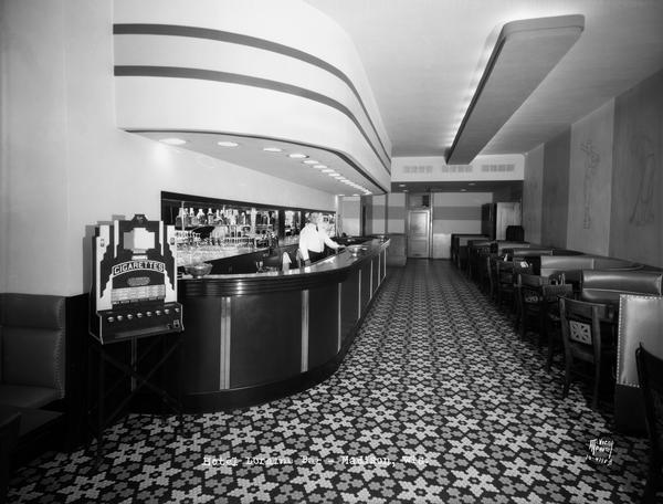 Art deco style bar in the Hotel Loraine at 119-125 West Washington Avenue, with an art deco cigarette machine. The bartender is standing at his post behind the bar.