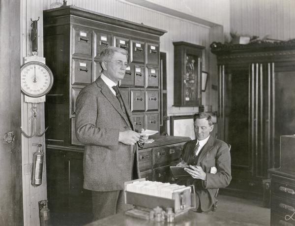Noted agriculture economist Henry C. Taylor standing with paper in hand, with seated unidentified man.