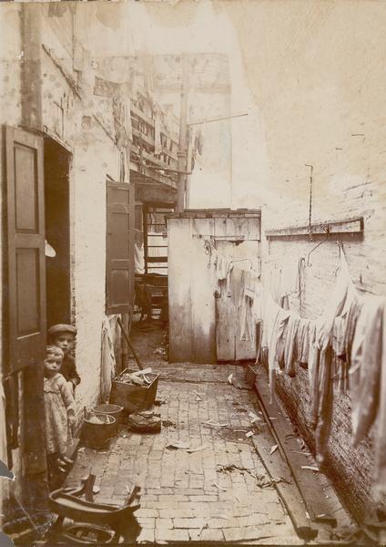 An entirely closed court in a tenement district. Two children are in a doorway.