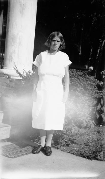 Full-length portrait of Zella Marie Eagen standing outdoors near a column wearing a white dress.