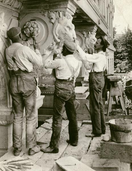 Three stone cutters (probably Italian) working on decorative details over the east entrance of the State Historical Society of Wisconsin (Wisconsin Historical Society) building.