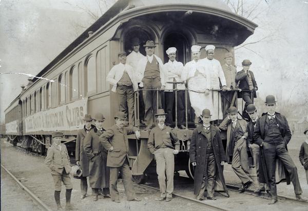 Members of the University of Wisconsin Glee, Banjo and Mandolin Club posing at the rear of a train during the Spring Tour of 1896. Railroad employees and other men are posing on the back of the caboose.