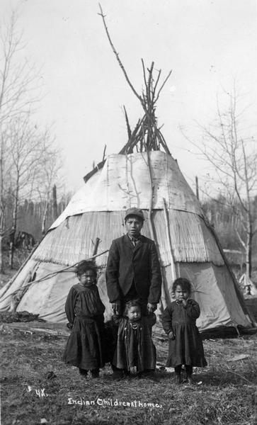 Four Indian children posing in front of a tipi on a Menominee Indian reservation.