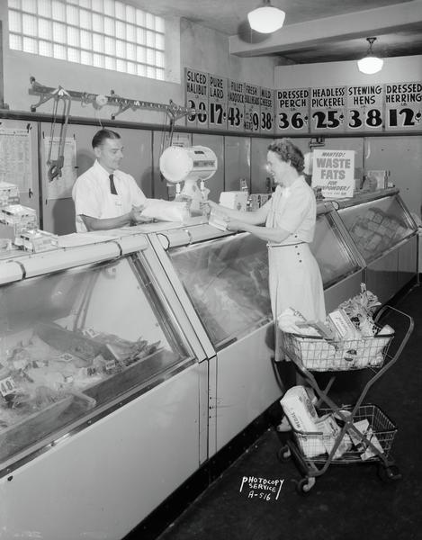 A woman shopping in the meat department at the Kroger store at Union Corners, 2541 Winnebago Street. She is there to promote the wartime Oscar Mayer Health for Victory Club. Marvin J. Leitzke, meat manager, is behind the meat case.