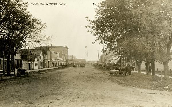 View down Main Street with horse-drawn wagons parked at the side of the dirt road.