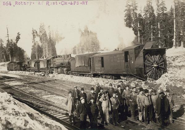 Elevated view of a group of men posing on railroad tracks in front of the 564 rotary snowplow engine at rest.