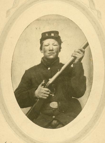 Studio portrait of Civil War soldier Syver (Sivert) Larson holding a rifle. He served as a Private in Company K of the 15th Wisconsin Volunteer Infantry. He was a resident of Emmet County, Iowa, when he enlisted on February  3rd, 1862. He was wounded and taken prisoner at Stone River, and was mustered out February 10th, 1865 with the remainder of his company.